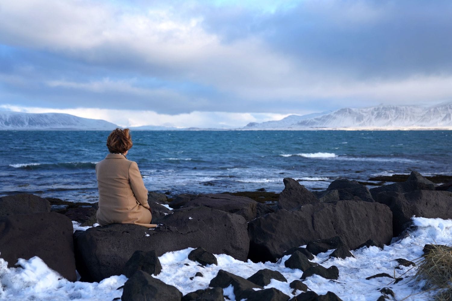 Kona situr og horfir á hafið