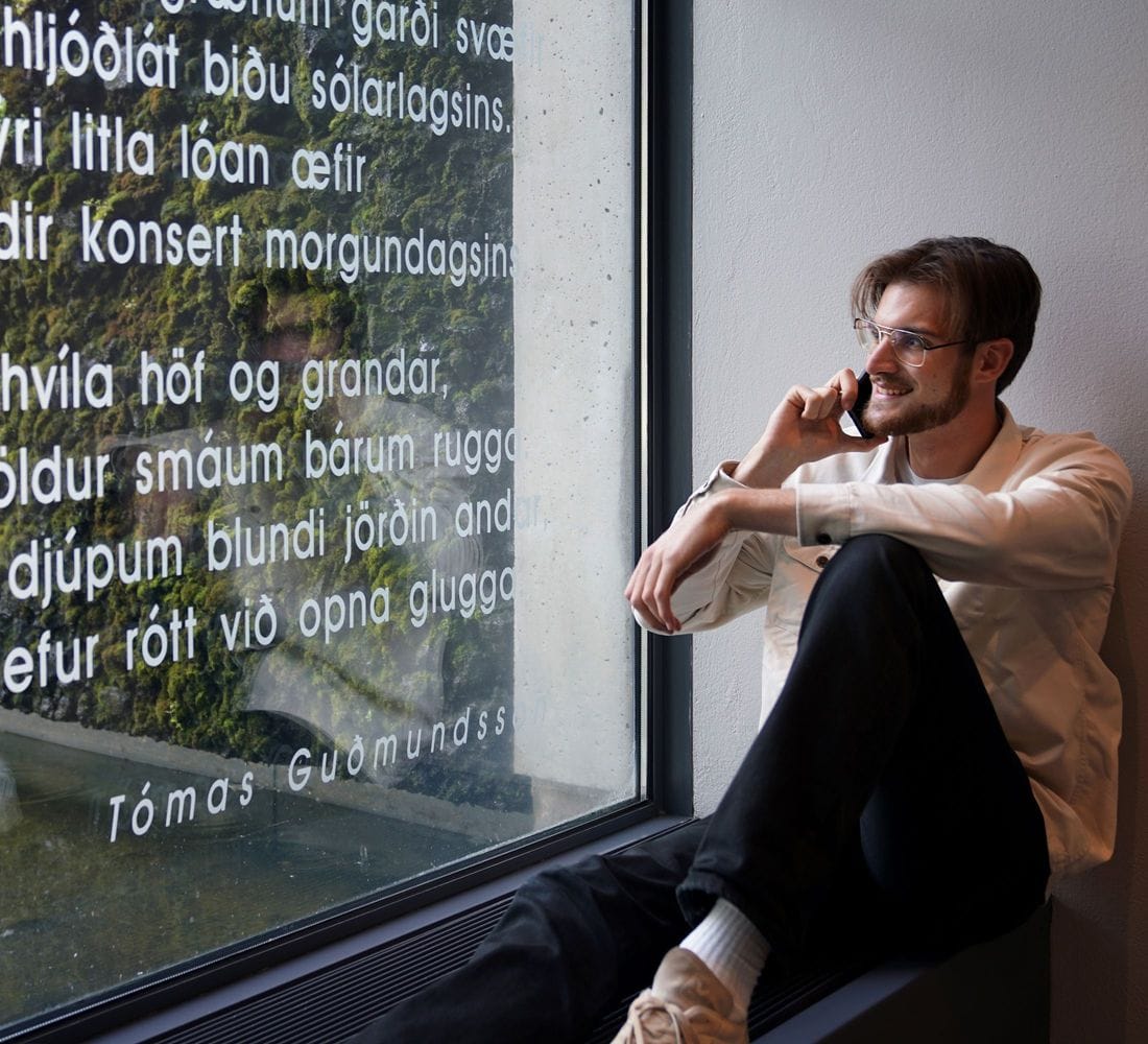 Ungur maður situr í glugga í símanum