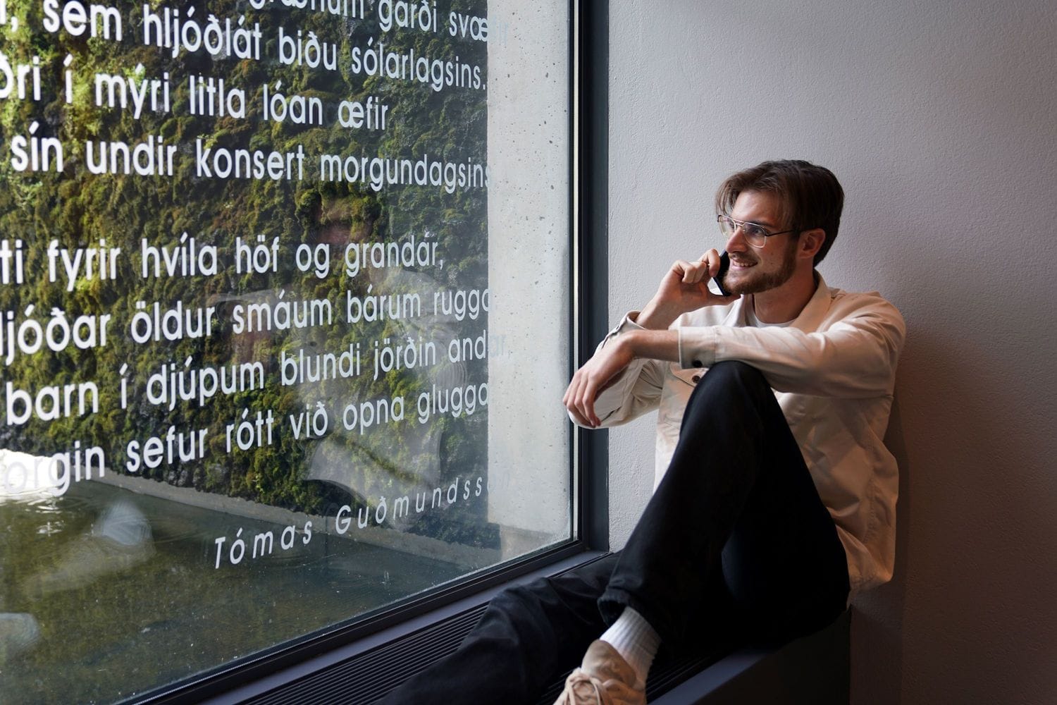 Ungur maður situr við glugga og talar í síma