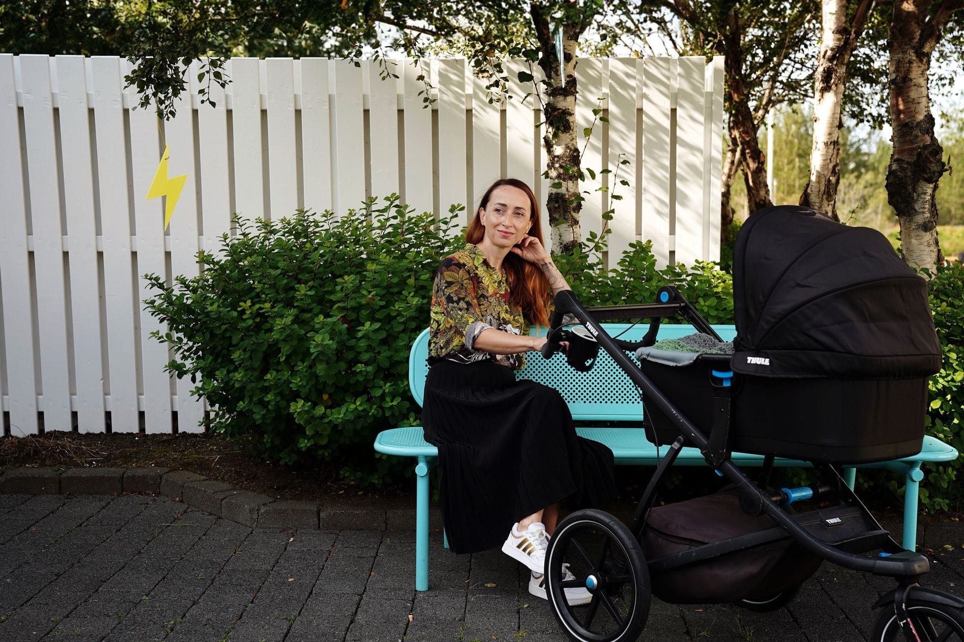 Ung kona sitjandi úti um sumar með barnavagn