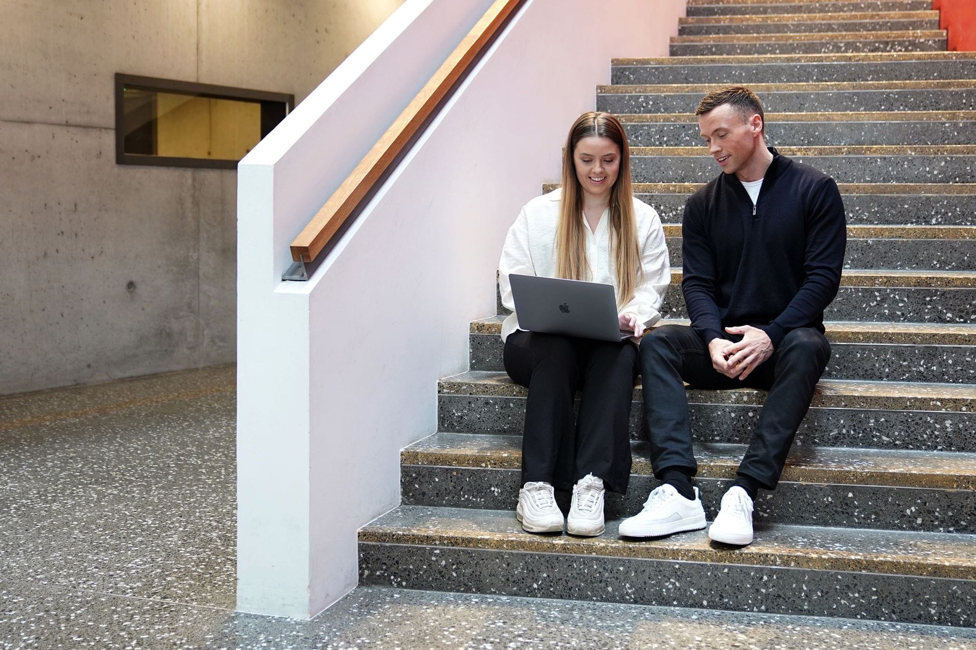 Ungt fólk situr saman í stiga og bendir á tölvu