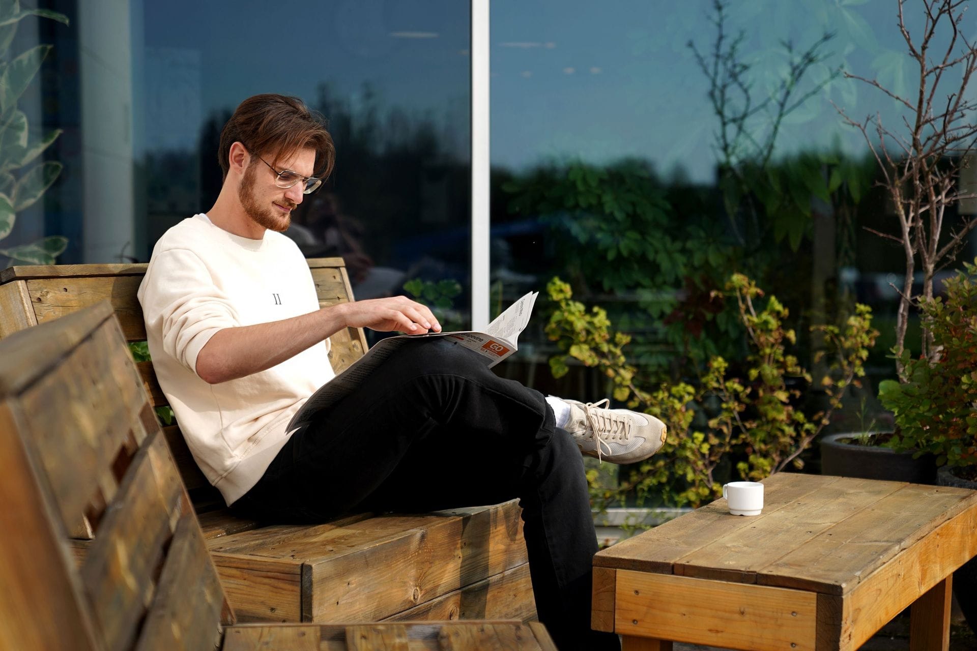 Ungur maður situr úti að drekka kaffi og lesa blað
