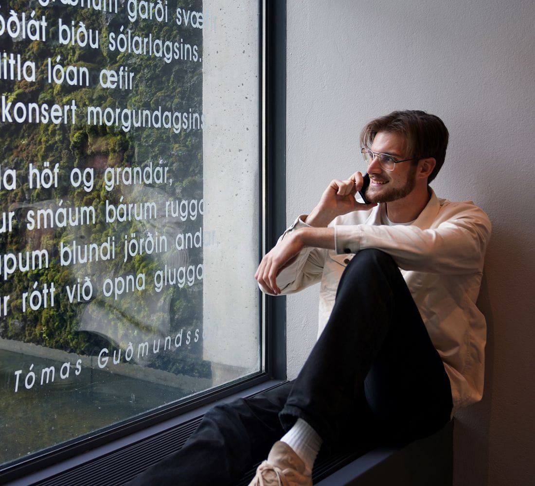 Ungur maður situr við glugga og talar í síma